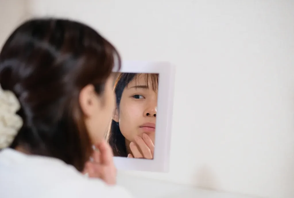 鏡を見て肌荒れを気にする女性